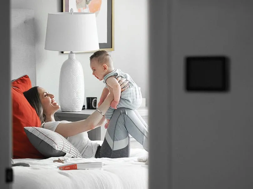 Family relaxing in a cool bedroom with an air conditioner thermostat nearby.