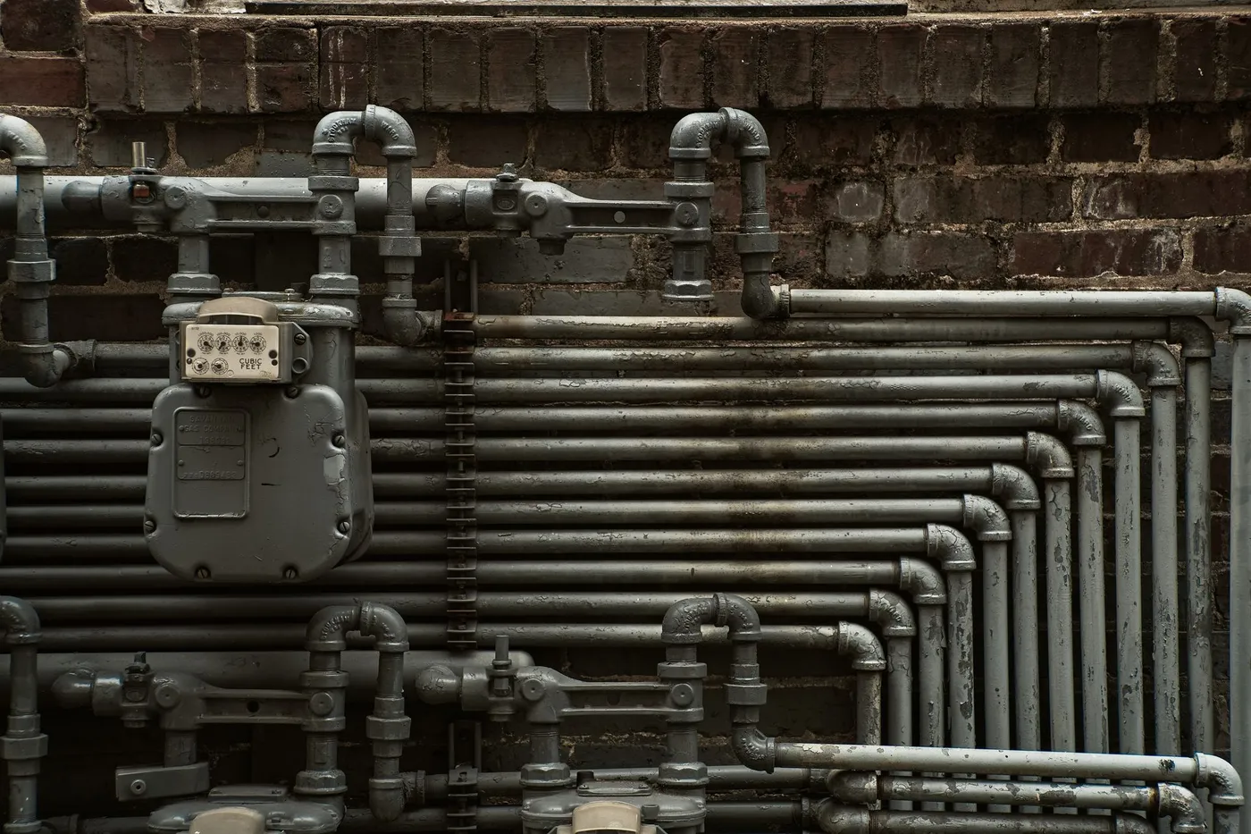Gas meter and black iron gas piping on a brick exterior wall.