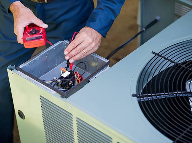 Technician inspecting HVAC unit with multimeter during maintenance service.